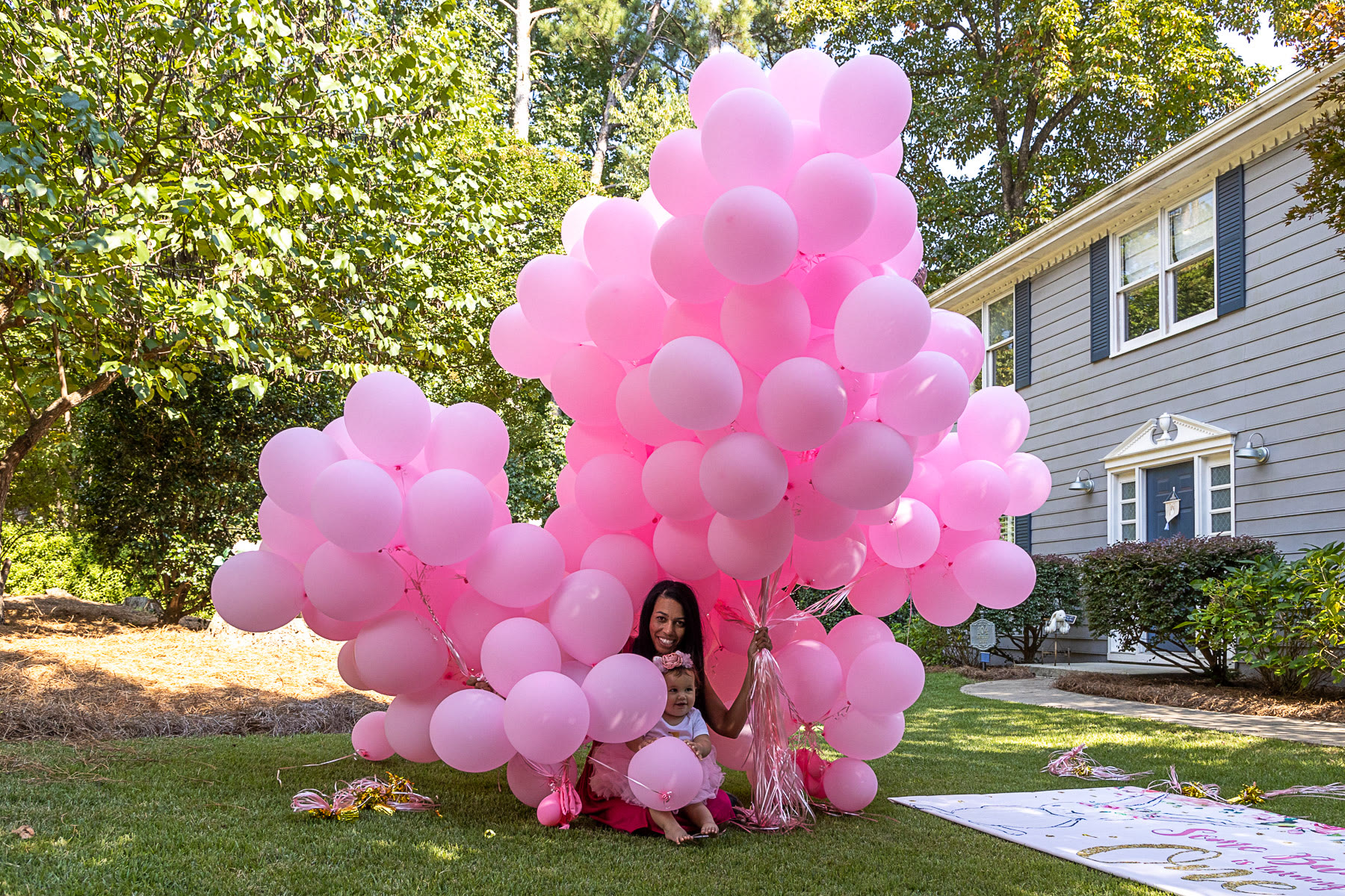 A giant bunch of pink balloons at an outdoor birthday celebration
